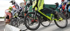 Gruppo di ciclisti BMX con caschi e abbigliamento protettivo colorato pronti sulla rampa di partenza di una gara BMX.