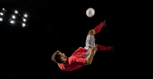 Calciatore in maglia rossa esegue una rovesciata durante una partita di calcio.