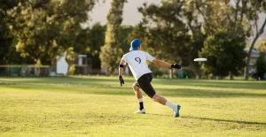 Persona che lancia un frisbee in un parco soleggiato, con maglietta bianca numero 9 e cappello blu.