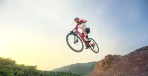 Persona che salta con una mountain bike su un percorso sterrato, indossando casco protettivo e abbigliamento sportivo.