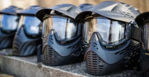 Caschi da paintball con visiera trasparente e protezione facciale nera allineati su superficie piana.