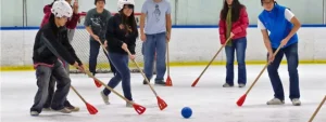 Persone che giocano su ghiaccio con mazze di plastica e una palla, indossando caschi e abiti invernali.