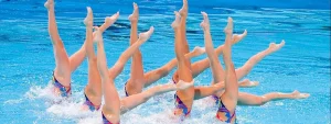 Atlete di nuoto sincronizzato eseguono una figura con gambe dritte sollevate in verticale in piscina, mostrando coordinazione e precisione.