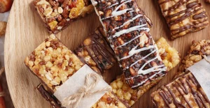 Selezione di barrette di cereali con cioccolato, noci e frutta secca su un piatto di legno, alcune avvolte in carta e legate con spago.