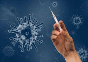 Mano che tiene una siringa davanti a uno sfondo blu con ingrandimenti stilizzati di virus, rappresentando la vaccinazione.