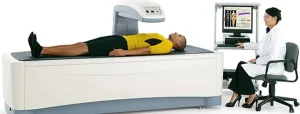Persona in abbigliamento sportivo sdraiata su macchina per densitometria ossea, con medico in camice bianco al computer che esegue la scansione ossea.