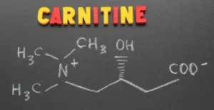 Parola "CARNITINE" colorata su sfondo scuro con diagramma chimico a gesso che rappresenta la struttura molecolare della carnitina