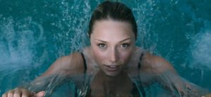 Persona che nuota sott’acqua vista frontalmente, circondata da bolle e schizzi mentre emerge in un ambiente acquatico blu.