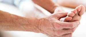 Persona che massaggia il piede di un’altra in un ambiente rilassante, con luce calda e contatto visibile tra mani e piede.