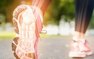 Primo piano di scarpe da ginnastica rosa con suola ammortizzata mentre una persona corre su un sentiero all’aperto in un parco con alberi verdi e luce solare.
