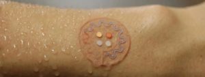 Braccio sudato con dispositivo circolare trasparente contenente sensori applicato sulla pelle per monitoraggio del sudore.