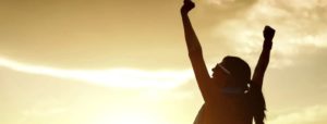 Silhouette di una persona con le braccia alzate verso il cielo al tramonto, in un gesto di vittoria e gioia, con colori caldi e dorati.