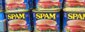 Lattine di Spam impilate con etichetta blu e logo giallo, raffigurante un panino con Spam, formaggio, pomodoro, lattuga e pane con semi di sesamo.