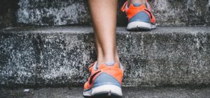 Parte inferiore delle gambe di una persona che sale scale in pietra, con scarpe da ginnastica arancioni e grigie.