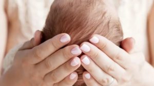 Neonato con la testa sostenuta da mani femminili curate con smalto chiaro, simbolo di protezione e dolcezza.