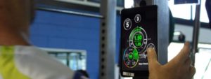Persona che monitora parametri di allenamento su tablet in palestra, con grafici e dati di velocità visibili sullo schermo.