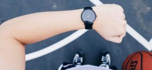 Braccio con orologio nero sopra una persona che tiene una palla da basket su un campo con linee bianche.