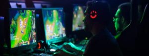 Gruppo di persone sedute a postazioni di gioco con cuffie e microfono, intenti a giocare a un videogioco strategico.
