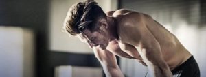 Uomo a torso nudo affaticato dopo esercizio fisico intenso in palestra.