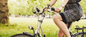 Parte inferiore del busto e gambe di persona su bicicletta con vestito scuro in parco verde soleggiato