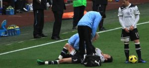 Giocatore a terra infortunato su un campo da calcio assistito da due membri dello staff medico.
