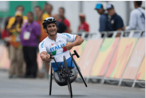 Alex Zanardi gareggia su handbike con la maglia "Italia" durante una competizione, con spettatori sullo sfondo