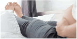 Persona distesa su un letto con i piedi sollevati, in una posa rilassata, con una mano sulla pancia.
