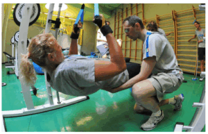 Donna sollevata con fasce da fitness mentre un uomo la assiste in palestra.