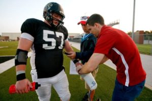 Giocatore di football americano numero 57 riceve una bottiglia da un assistente sul campo.