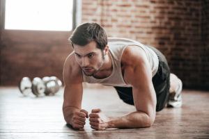 L'immagine ritrae un uomo durante un esercizio di plank, in un ambiente domestico o da palestra con atmosfera rustica. La scena comunica concentrazione, forza e allenamento funzionale, ideale per contenuti su fitness e core training.