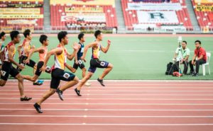 Atleti che corrono velocemente in una gara di atletica leggera su pista, con spettatori e ufficiali ai lati