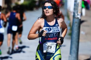 Donna in gara di triathlon con tenuta sportiva "CLUB TRIATLON JAEN" e numero 79, capelli bagnati e occhiali da sole, concentrata in movimento.