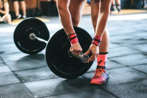 Persona in palestra con scarpe da ginnastica colorate e calzini rosa regola i pesi su un bilanciere su pavimento a piastrelle nere.