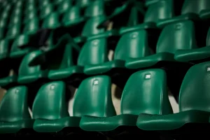 File di sedili verdi vuoti in uno stadio ripresi in prospettiva obliqua con effetto di profondità di campo.