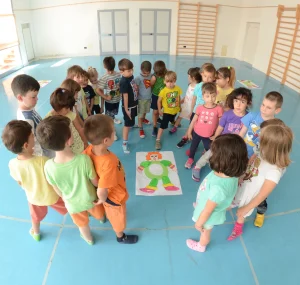 Bambini in cerchio durante un’attività educativa in palestra osservano un disegno del corpo umano al centro del pavimento.