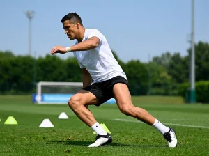 Atleta durante un esercizio di rapidità su un campo da calcio, inclinato in avanti mentre cambia direzione, con coni di allenamento visibili sull’erba.