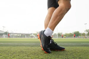 Gambe e piedi di un calciatore con scarpini da calcio su campo in erba sintetica durante una sessione di gioco o allenamento