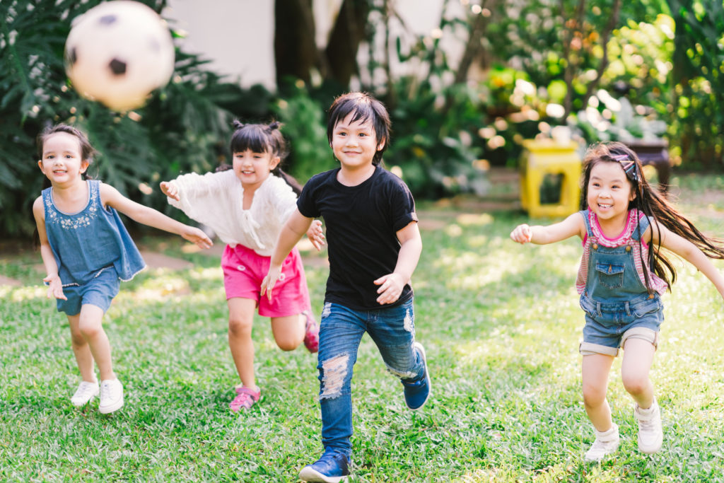 Gruppo di bambini che corrono e giocano a calcio in un prato, esempio di attività fisica aerobica che favorisce la neuroplasticità e il sano sviluppo cognitivo infantile.