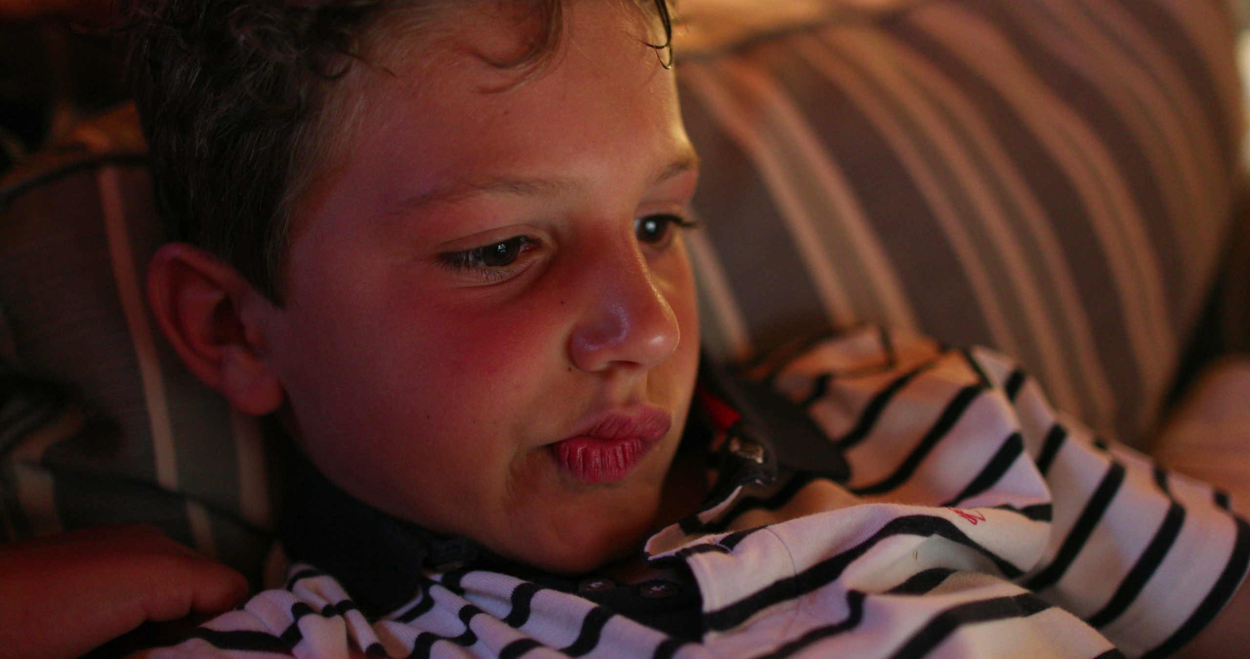 Primo piano di un bambino al buio illuminato dalla luce blu di uno schermo, a illustrare il rischio di sovra-stimolazione sensoriale e l'interferenza con lo sviluppo cognitivo infantile.